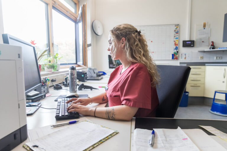 Pflegefachkraft tippt am Computer Dokumente im Büro ein.