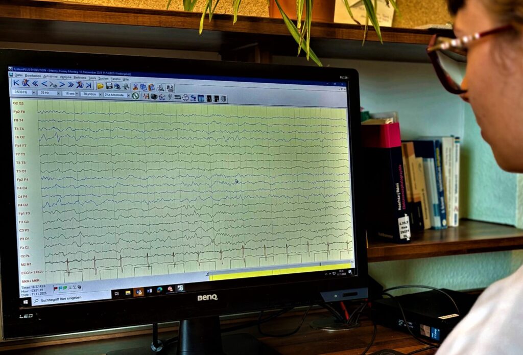 Medizinische Fachkraft wertet die Kurven eines EEG-Protokolls am Computermonitor aus.