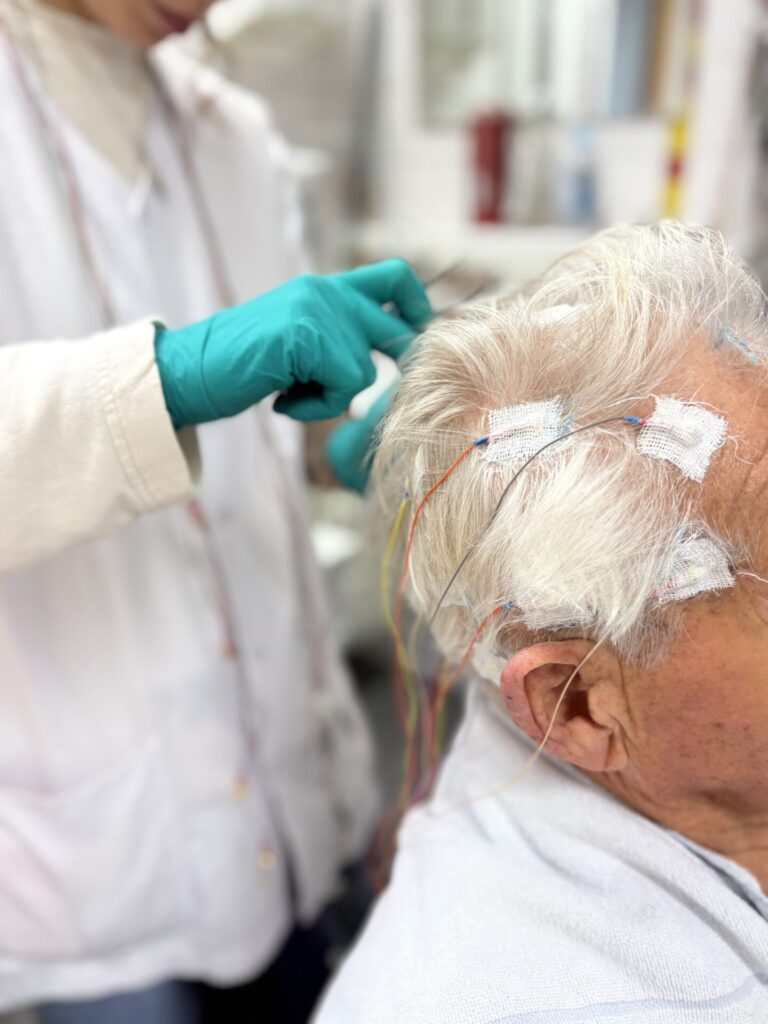 Fachkraft befestigt Elektroden am Kopf des älteren Patienten.