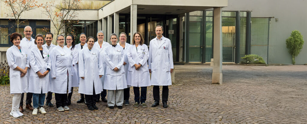 Gruppe von Ärztinnen und Ärzten im weißen Kittel steht vor dem Eingangsbereich einer Klinik und blickt lächelnd in die Kamera.